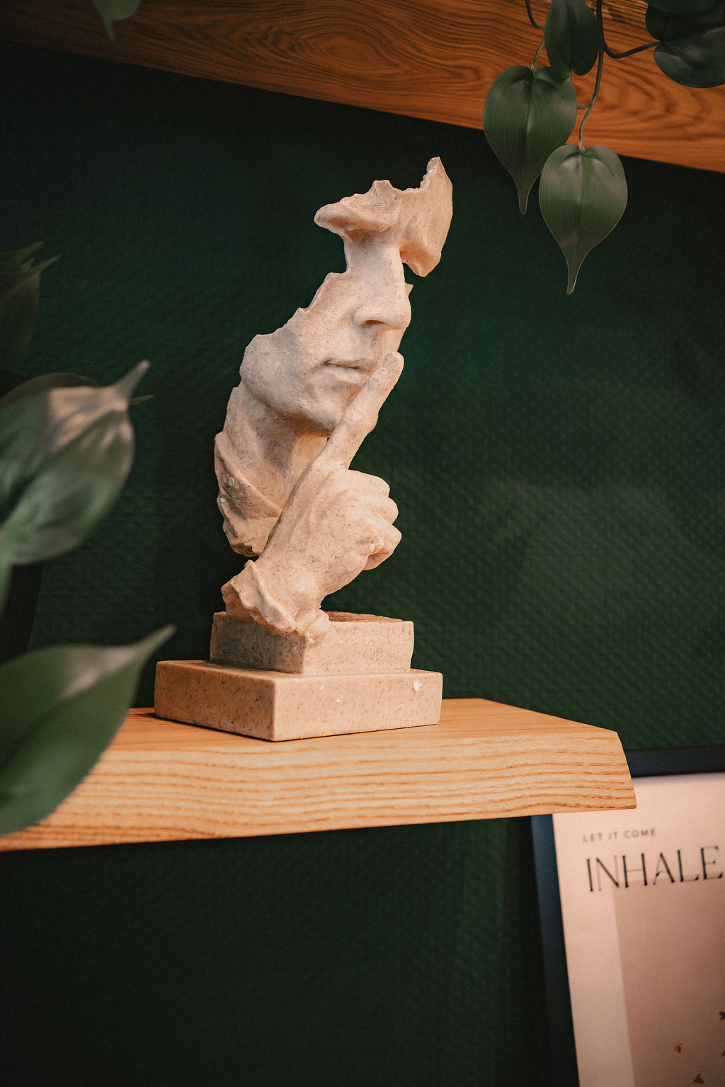 Weiße Skulptur eines Gesichts, teilweise von Blättern umgeben, auf einem Regal.