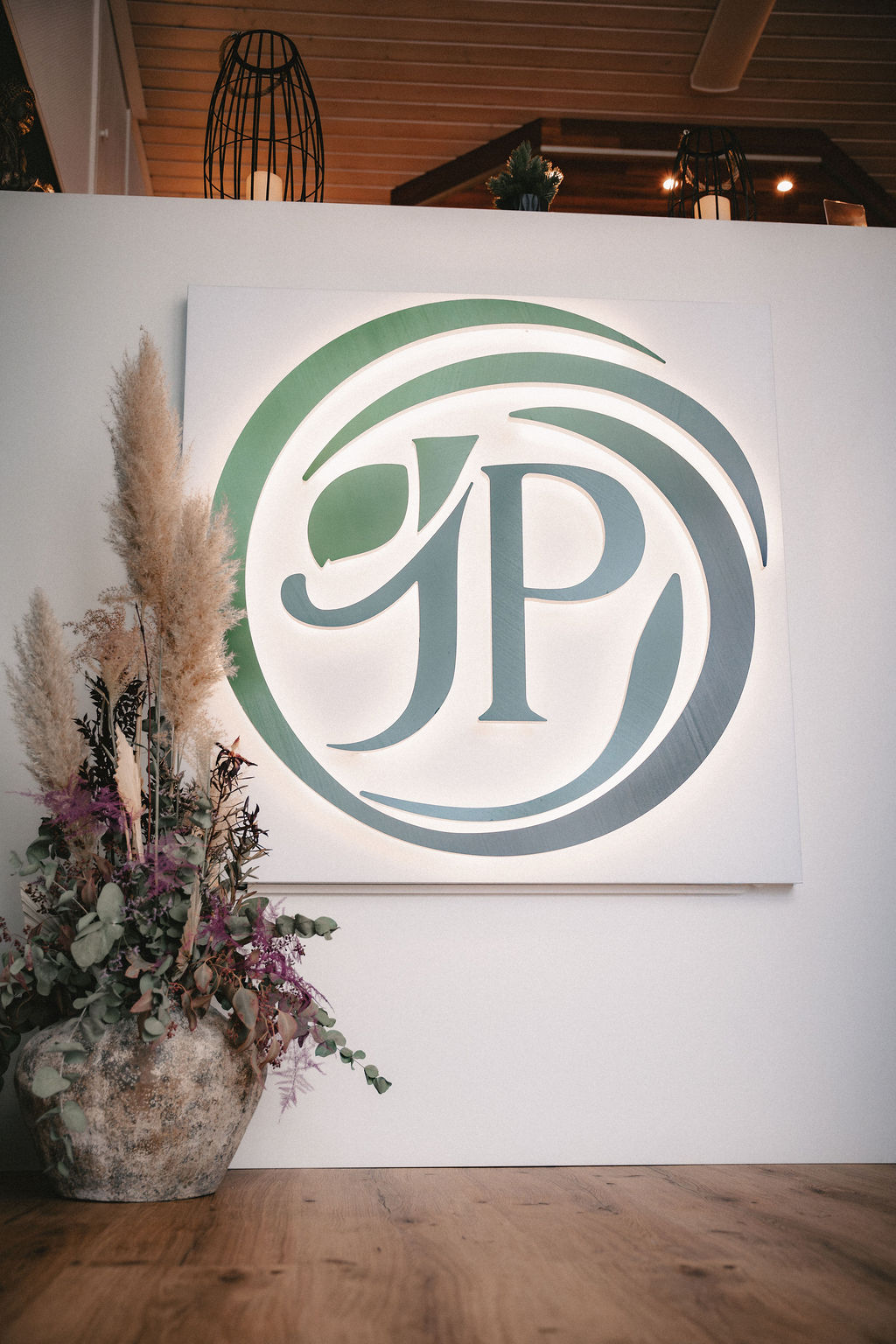 Logo von GP mit geschwungenen Linien und dekorativen Pflanzen im Vordergrund.