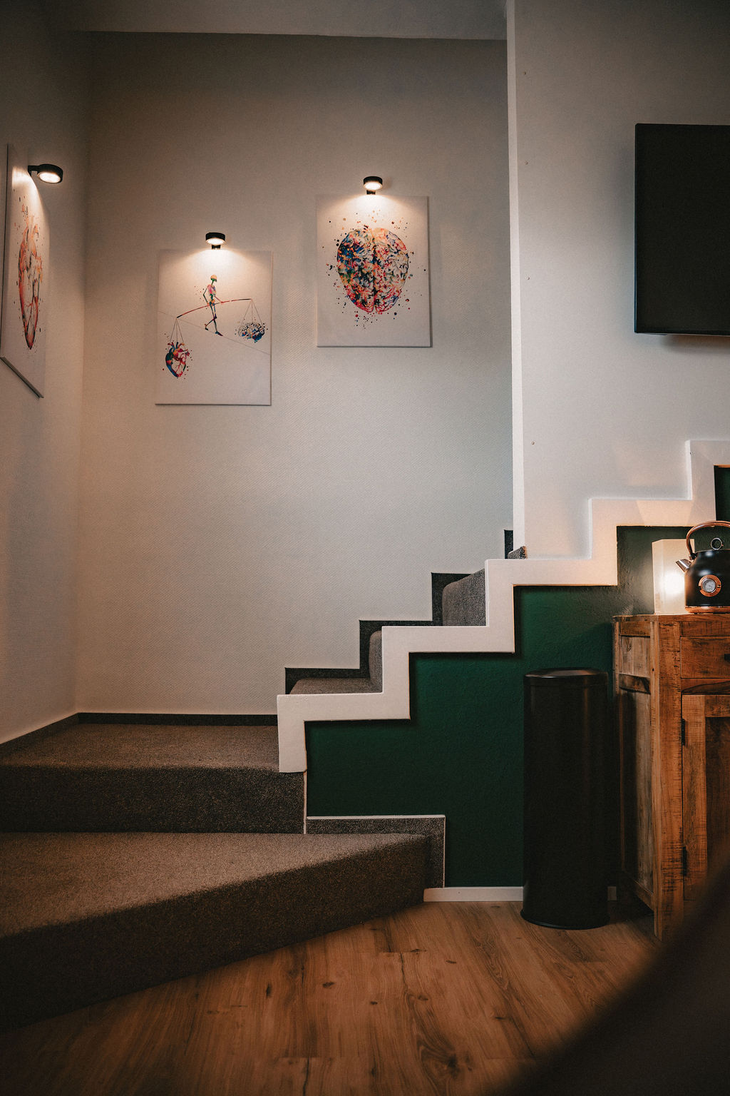 Treppenaufgang mit Kunstwerken an der Wand und dezenten Lampen.