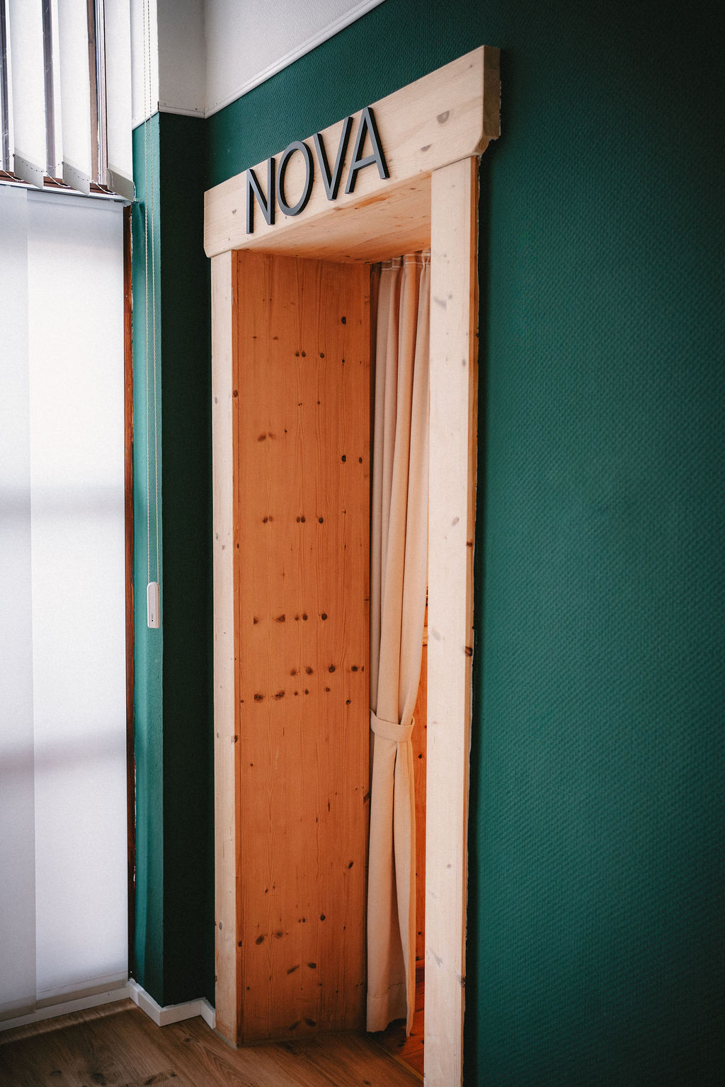 Holztürrahmen mit dem Schriftzug "NOVA" und hellen Vorhang in einem grünen Raum.