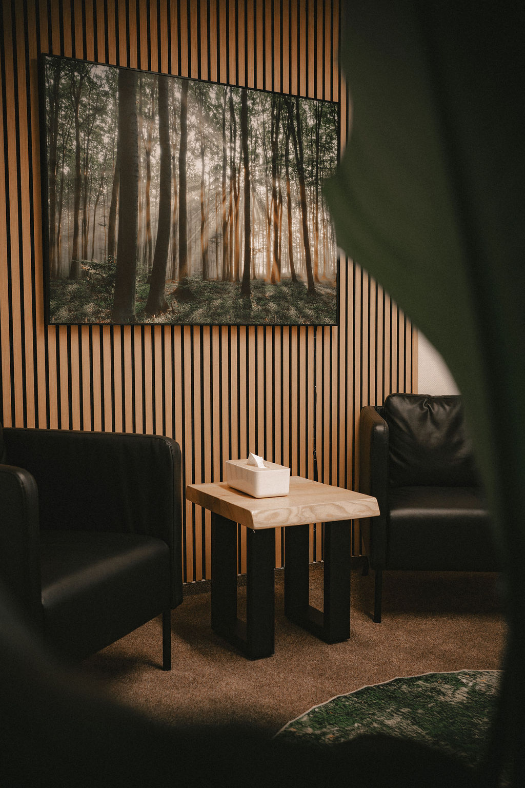 Zwei schwarze Ledersofas stehen neben einem Tisch in einem Raum mit Waldmotiv an der Wand.